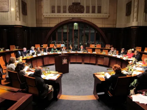 Etwa 20 Personen sitzen kreisförmig hinter Pulten im Hodlersaal.