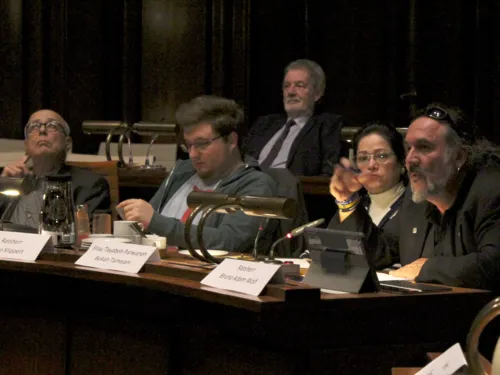 Vier Personen sitzen nebeneinander im Hodersaal des Neuen Rathause. Ein Mann ganz rechts sitzend spricht.