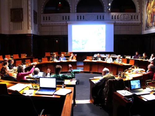 Die Ausschussmitglieder sitzen im Hodlersaal im Kreis hinter Pulten. Drei heben die Hand zur Abstimmung.