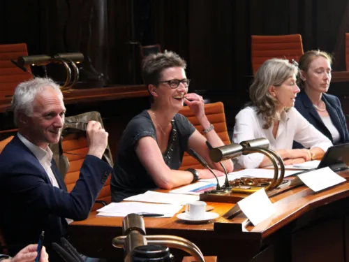 Vier Personen sitzen im Hodlersaal nebeneinander hinter Pulten. Der mann und die Frau, die links sitzen, blicken nach vorne und lachen.