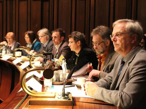 Sieben Personen - zwei Frauen und fünf Männer - sitzen im Hodlersaal nebeneinander hinter Pulten