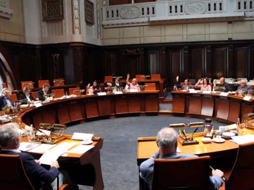 Etwa 12 Personen sitzen im Hodlersaal hinter Pulten. Einige davon heben die Hand zur Abstimmung hoch.