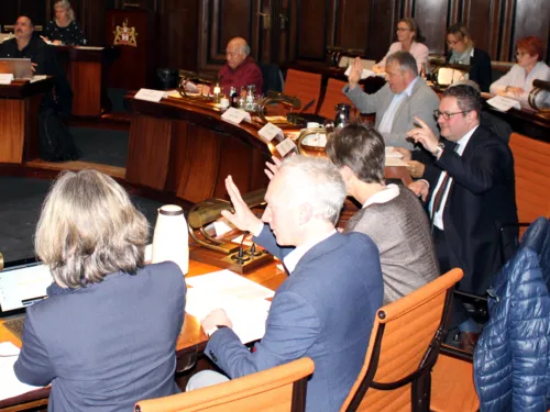 Etwa zehn Personen sitzen an kreisförmig aufgestellten Pulten im Hodlersaal des Neuen Rathauses. Drei davon heben den Arm zur Abstimmung.
