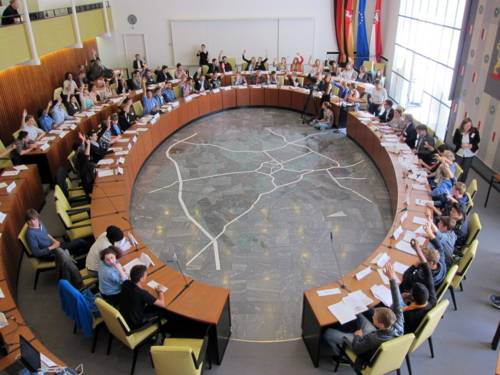 Alle teilnehmenden Sch&uuml;ler/innen im Ratssaal. Die meisten heben die Hand zur Abstimmung.