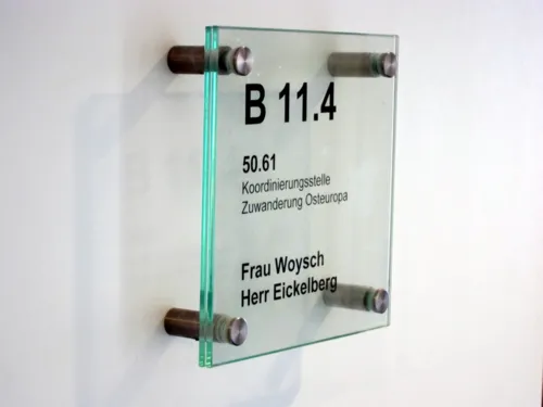 Foto eines transparenten Büroschildes, auf dem steht "Koordinierungsstelle Zuwanderung Osteuropa und die Namen "Frau Woysch" und "Herr Eickelberg".