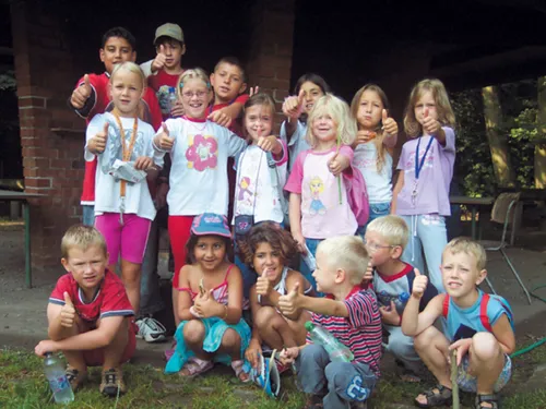 Eine Gruppe Kinder hält vor einem Familienzentrum die Daumen hoch
