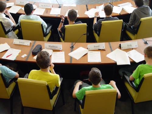 Blick von oben auf einige Jugendliche, die im Ratssaal der Landeshauptstadt Hannover sitzen. Vor den Jugendlichen liegen verschiedene Dokumente auf den Tischen.