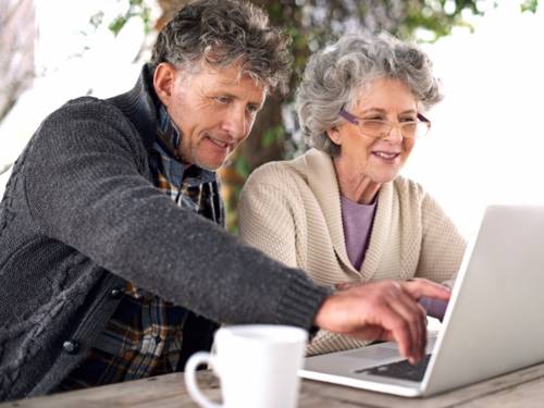 Eine ältere Dame mit Brille und ein Mann sitzen vor einem Laptop