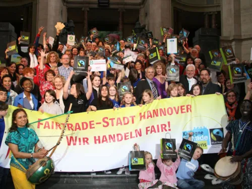 Gruppenbild mit zahlreichen Aktiven allen Alters auf der Rathaustreppe, die ein Transparent mit der Aufschrift "Fairtrade-Stadt Hannover - wir handeln fair" in den H&auml;nden halten.