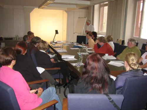 Teilnehmende der Arbeitsgruppe sitzen an einem langen Tisch und hören einen Vortrag