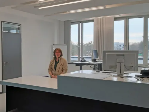 Eine freundliche Mitarbeiterin steht an einem Arbeitsplatz.
