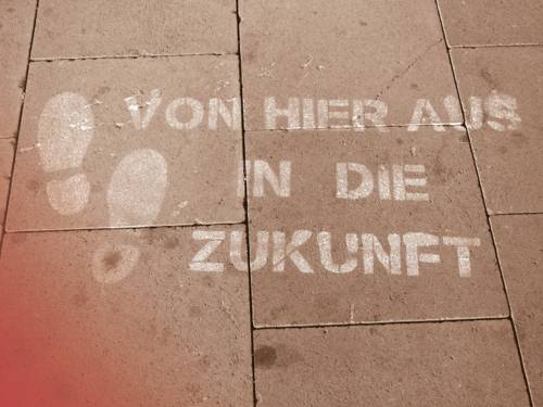 Auf einem gepflasterten Weg sind zwei Fußabdrücke aufgebracht, daneben der Schriftzug "Von hier aus in die Zukunft".