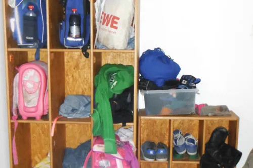 In einem Holzregal sind Rucksäcke und Schuhe von Kindern und Jugendlichen verstaut.