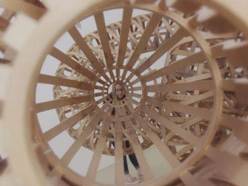 Eine junge Frau schaut durch eine spiralförmige Holzkonstruktion