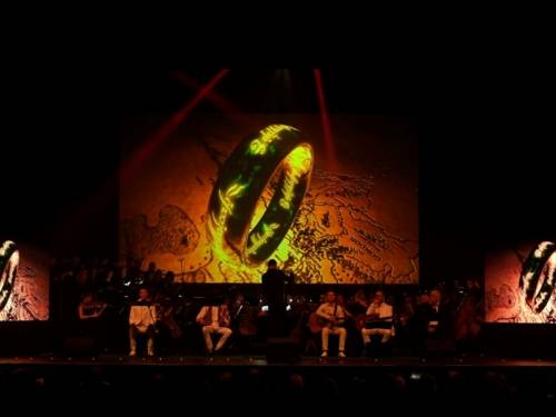 Das Orchester sitzt vor einer großen Leinwand mit einem Ring darauf. 