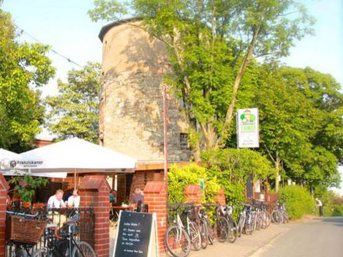 Menschen sitzen auf Bänken an Tischen vor einen historischen Turm.
