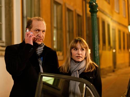 Ein Mann und eine Frau stehen an einer geöffneten Autotür, der Mann telefoniert mit einem Mobiltelefon.