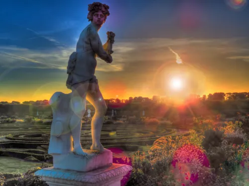 Sonnenuntergang in einer Gartenlandschaft, im Vordergrund links stehe eine Statue.