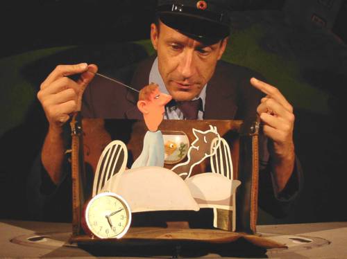 Achim Fuchs-Bortfeldt vom Figurentheater Die Füchse steht hinter einen kleinen Bühne und spielt mit einer Pappfigur, die sich aus ihrem Bett erhebt.