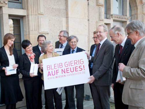 Menschengruppe mit Plakat mit dem Schriftzug: Blieb Gierig, Auf ein Neues. www.wissen.hannover.de