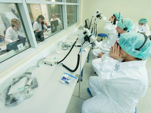 Mehrere Menschen in weißen Kitteln und mit Hauben auf den Köpfen, auf einem langen Tisch stehen Geräte