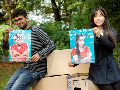 Eine Frau und ein Mann halten jeweils ein Plakat mit frierenden Menschen im Regen und der Aufschrift "Lasst uns nicht im Regen stehen".