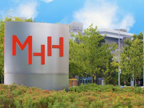 Eine Säule mit den Buchstaben "MHH", im Hintergrund Gebäude.