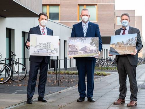 Drei Männer mit Nasen-Mundschutz-Masken halten Bilder in den Händen