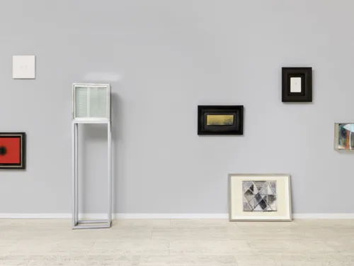 Gerahmte Bilder in verschiedenen Größen und unterschiedlichen Aufhängehöhen an einer Wand.
