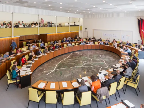 Saal mit elipsenförmig angebrachtem Tisch, an dem Menschen sitzen