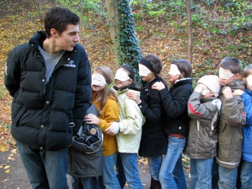 Betreuer führt Kinder mit verbundenden Augen durch den Wald