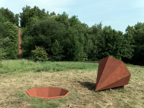 Aus dem grasbewachsenen Boden scheint ein achteckiger Kegel ausgestochen zu sein, der neben dem Loch liegt.