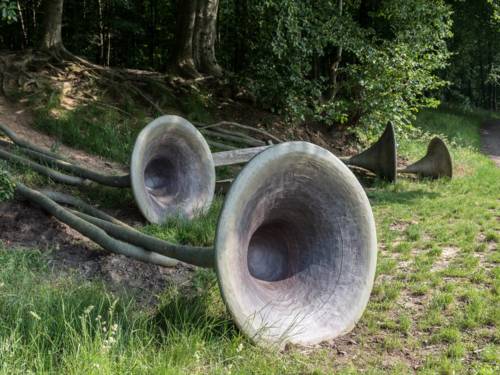 Aus Baumwurzeln an einem Hügel scheinen Klangtrichter zu wachsen, die an Alphörner erinnern.