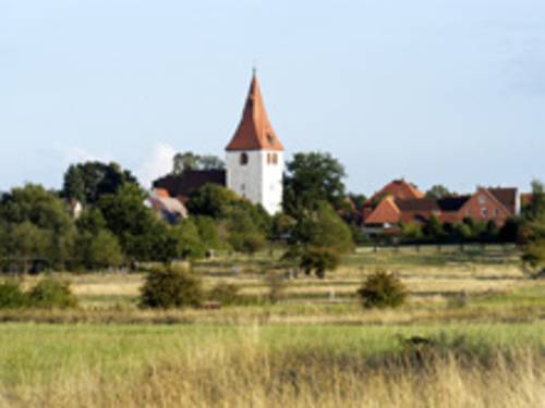 Landschaft mit Dorf und Kirchturm im Hintergrund.