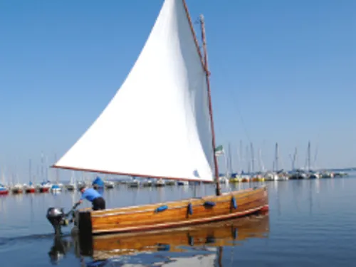 Ein Auswandererboot, eine offene Segeljolle, fährt als Ausflugsboot auf dem Steinhuder Meer.