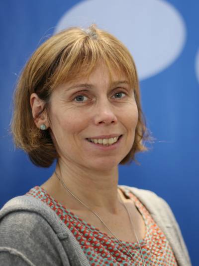 Porträtfoto von Sylvia Thiel vor einem blauen Hintergrund.