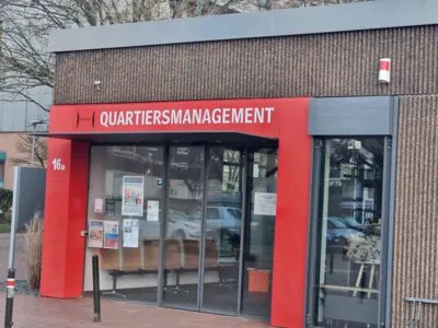 Auf dem Bild ist ein gro&szlig;er roter Eingang zu sehen mit dem Schriftzug "Quartiersmanagement"