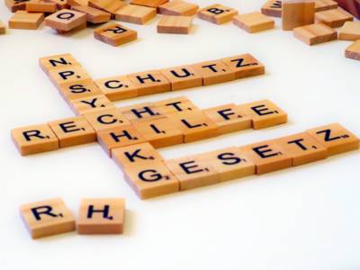 Kleine Holzplättchen sind für ein Legespiel mit einzelnen Buchstaben bedruckt. Die Holzplättchen legen die Worte: NPSYCHKG, Schutz, Recht und Gesetz.