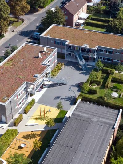 Luftaufnahme eines Gebäudekomplexes, auf dem Außengelände sind Spiel- und Sportgeräte.