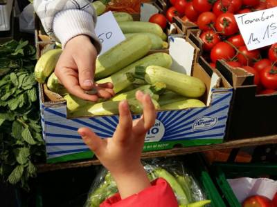 Die Hand eines Kindes, das an einem Gemüsestand steht, nimmt vom Händler Wechselgeld entgegen.