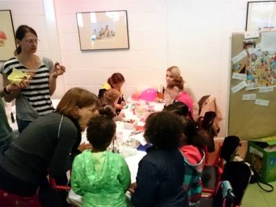 Eine Gruppe von Kindern bastelt zusammen an einem Tisch. Erwachsene beaufsichtigen die Kinder dabei.
