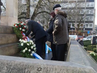 Menschen stehen vor einem Holocaust-Mahnmal und legen Blumenkr&auml;nze nieder. 