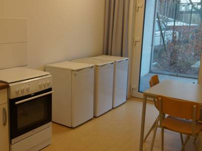 Eine Küchenzeile mit 3 Kühlschränken und einem kleinen Tisch mit Stuhl.