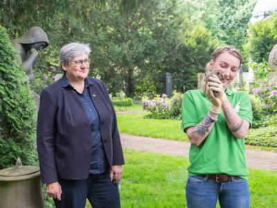 Zwei Frauen stehen auf einem Friedhof, eine der beiden h&auml;lt einen Igel in den H&auml;nden