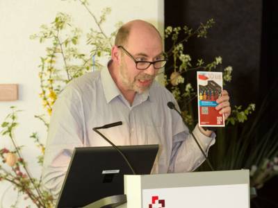 Friedhelm Hagen vom Fachbereich Soziales der Landeshauptstadt hält am Rednerpult eine Broschüre zum Thema Wohngeld in die Höhe