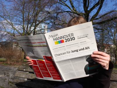 Ein junge Frau sitzt auf einer Parkbank und liest in einer Zeitung