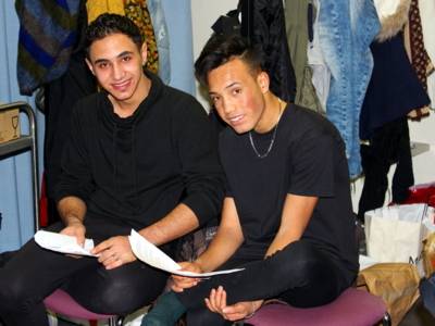 Zwei Jugendliche sitzen nebeneinander in einer Garderobe und halten Papiere in der Hand.