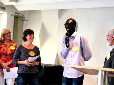 Vier Personen stehen auf einer B&uuml;hne. Eine davon spricht.