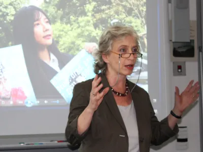 Eine Frau steht vor der Projektionsfl&auml;che eines Beamers und spricht.