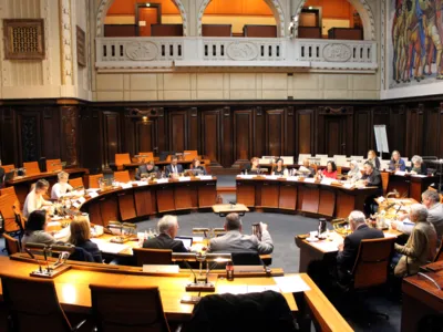 Etwa 15 Personen sitzen an kreisf&ouml;rmig aufgestellten Pulten.
